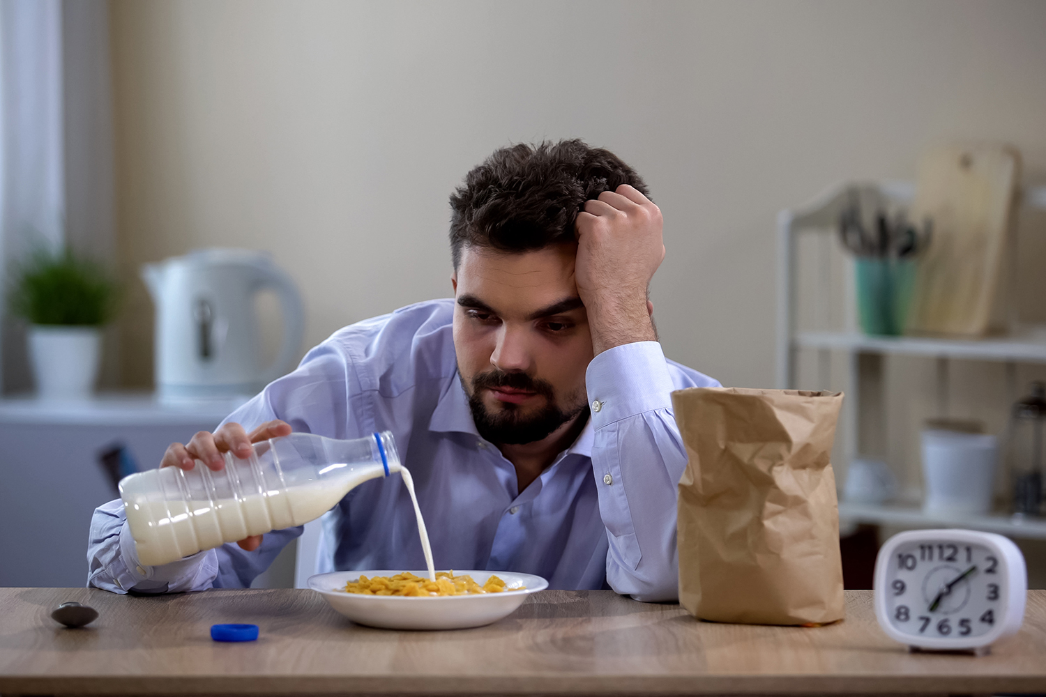 a very tired man pouring milk on his breakfast cereal