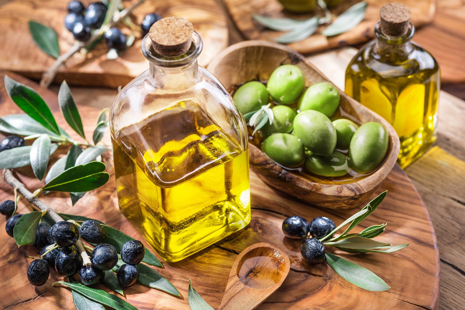 Olive oil, Berries on a branch and olives in a bowl placed on a wooden cutting board.
