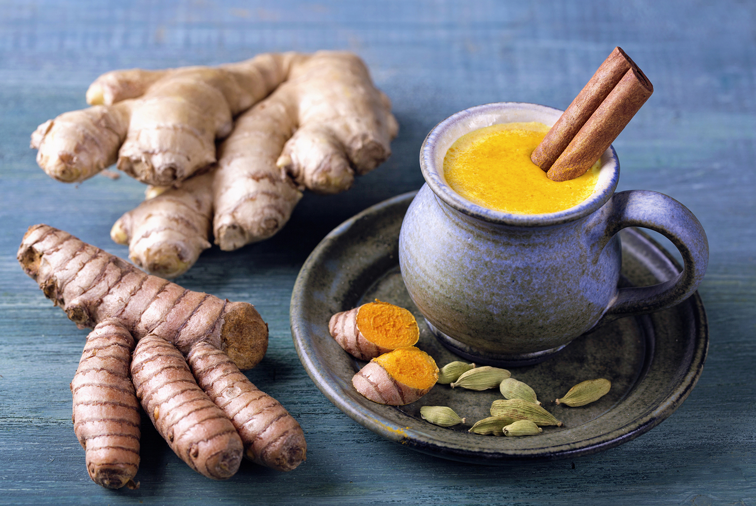 A mug of Golden Milk with turmeric and ginger root beside it.