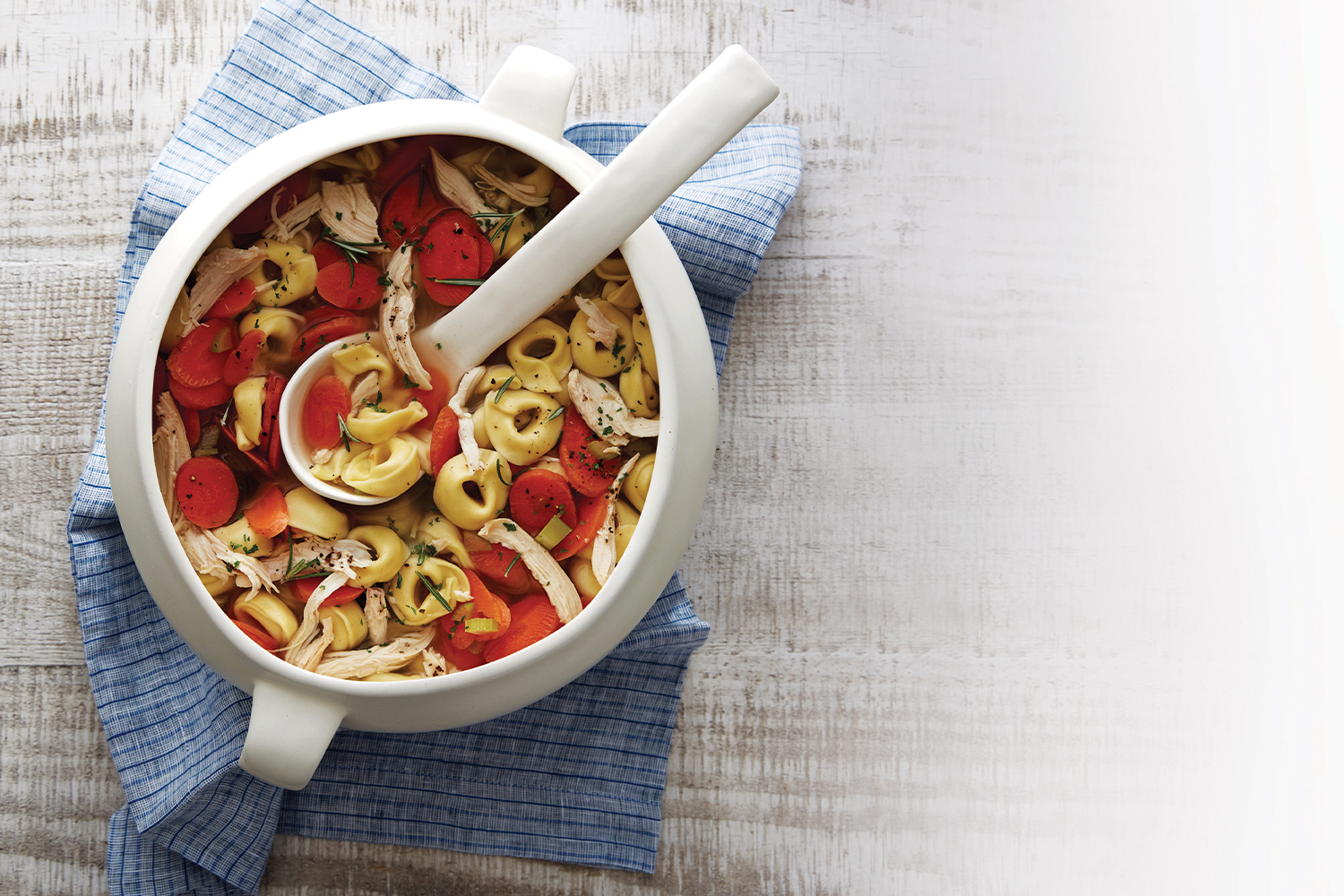 Chicken tortellini soup in a white soup crock.