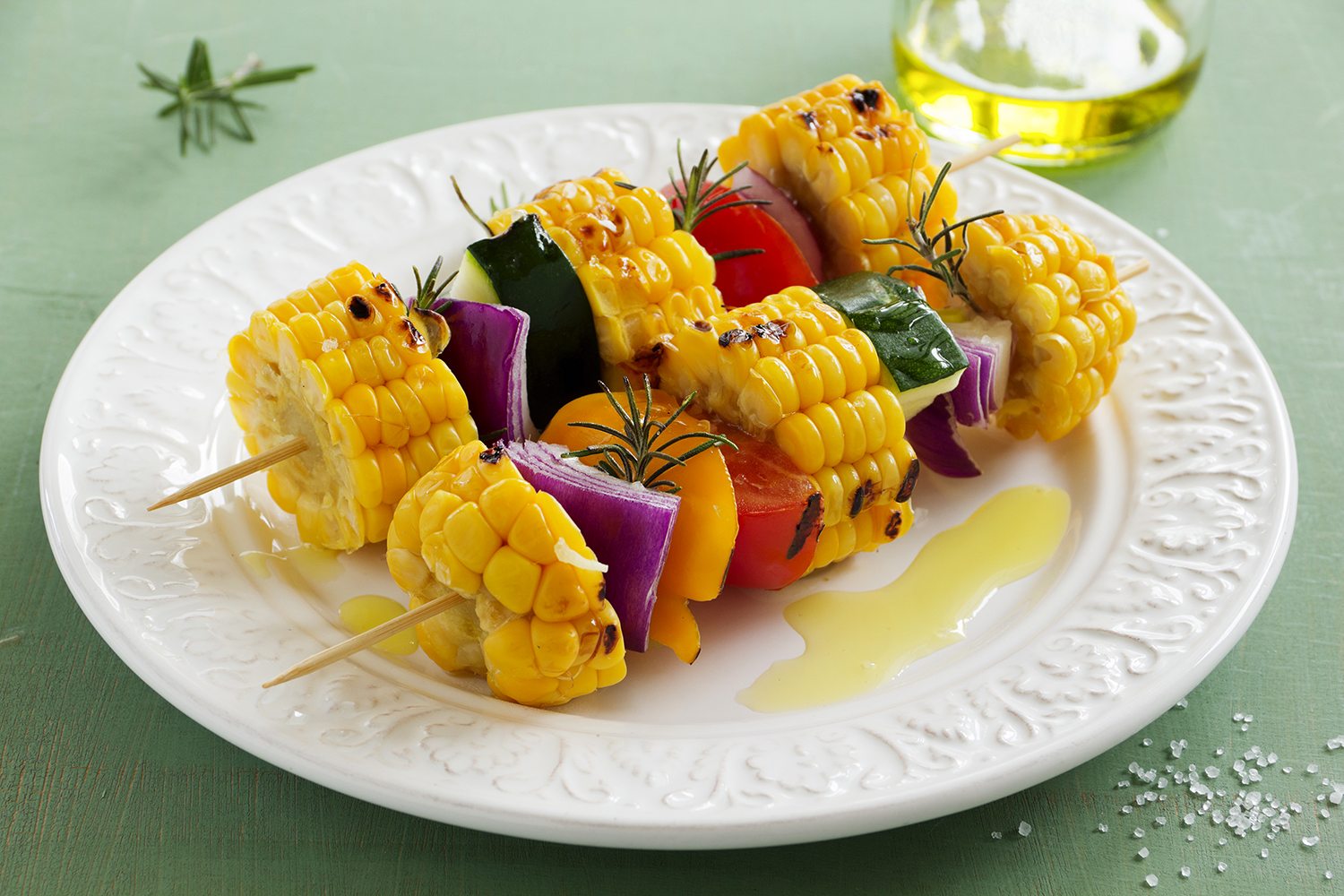 a plate of grilled vegetables on skewers with oil and seasoning