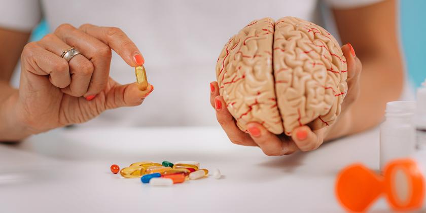 a woman holding a model brain and healthy supplements