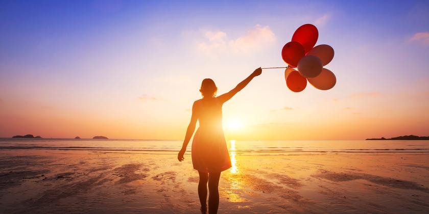 a happy woman holding balloons on the beach at sunset