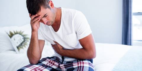 A man sitting on his bed with stomach discomfort.