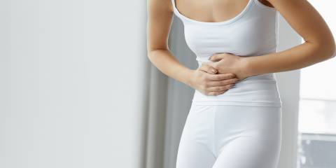 A woman in all white holding her stomach in pain.