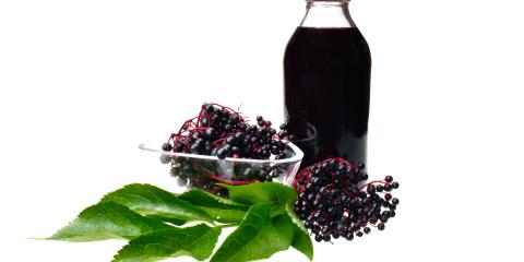 A glass jar of elderberry juice beside elderberry fruit bunches.