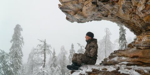 Man dressed in camouflage and a hat meditating on a mountain in winter. 
