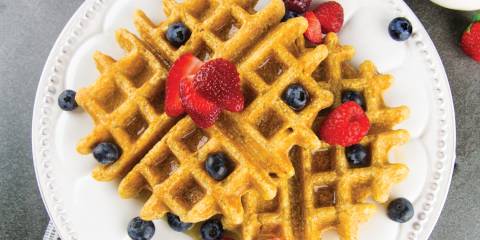 a plate of waffles with fruit and maple syrup