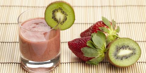 a glass of smoothie next to fresh strawberries and kiwi