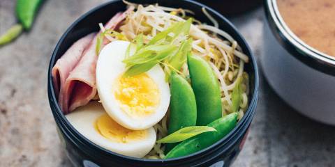 a bowl of noodles topped with ham, egg, and snow peas