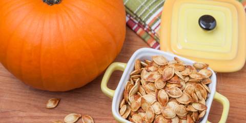 Roasted pumpkin seeds in a container next to a pumpkin. 