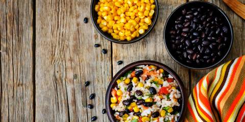 Fiesta salad, corn and black bean displayed in separate bowls. On a rustic farm table.