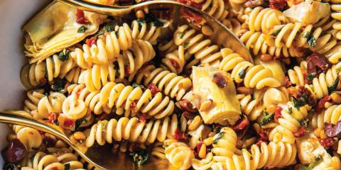 a bowl of fusilli with spinach, artichokes, and sun-dried tomatoes