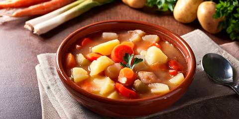 a bowl of soup with carrots, potatoes, and onions