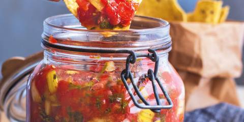 A tortilla chip dipped in a jar of fermented garden salsa