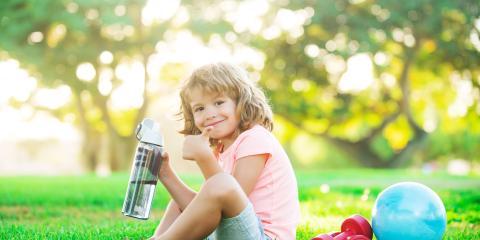 Kid with a water bottle sitting on the grass outside. 